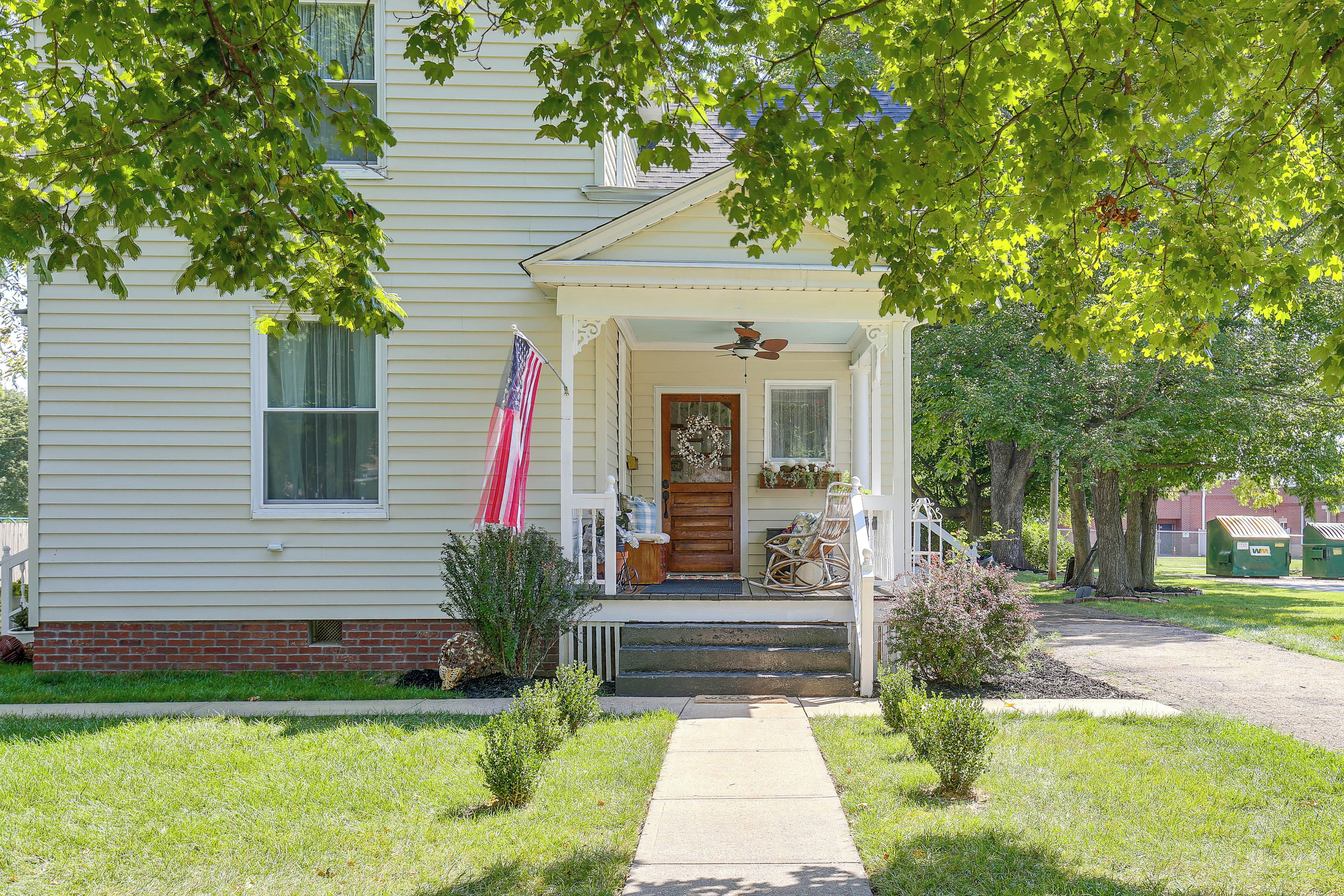 A two-story house with a front porch, a flag, and a mailbox.