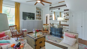 A living room with a television, bookshelves, a blue dresser, and a ceiling fan. - Shop, Dine, Explore Dtwn! Walkable Farmington Home (Farmington)