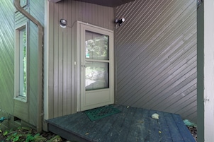 A wooden door with a window, a small porch with a green mat, and a wall with diagonal siding.