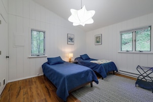 A room with two beds, a window, a door, and a hanging light fixture.