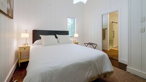 Un dormitorio con una cama grande, dos lámparas de noche, una ventana y una puerta que da a un baño.