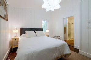 Quarto com uma cama grande, duas luminárias de cabeceira, uma janela e uma porta para um banheiro.