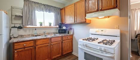 A kitchen with wooden cabinets, a white stove, a microwave, and a window with curtains.