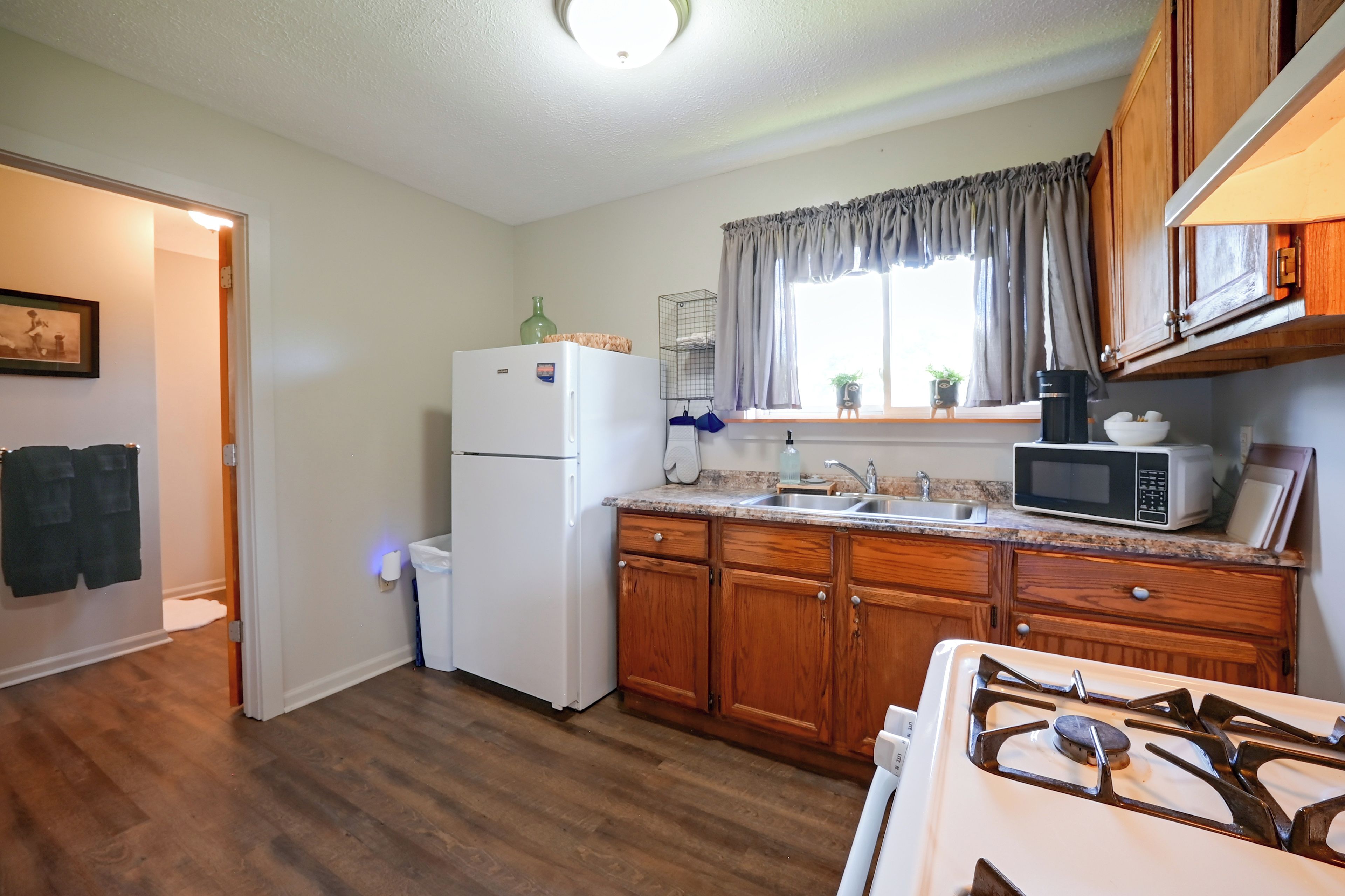 A compact kitchen with wooden cabinets, a white refrigerator, a microwave, and a gas stove.