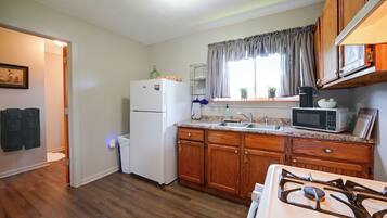 A compact kitchen with wooden cabinets, a white refrigerator, a microwave, and a gas stove.