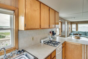 Una cocina con armarios de madera, estufa a gas, lavamanos y ventana con vista al agua.