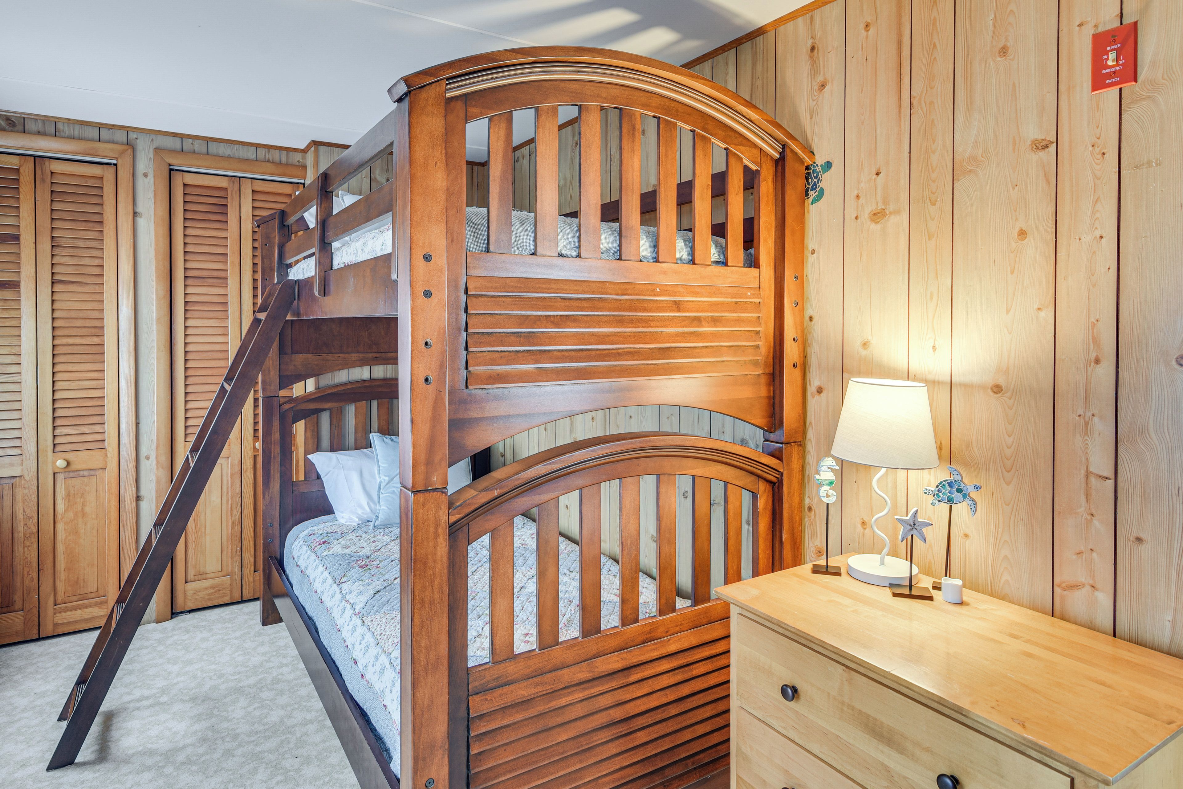 Uma cama beliche com escada, uma mesinha de cabeceira com abajur e paredes de madeira.