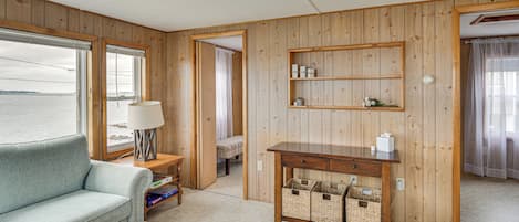 Una habitación con un panel de madera, un sofá, un escritorio con cestas de almacenamiento y vista al mar a través de una ventana.