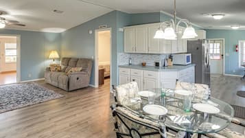 A spacious living area with a sofa, a dining table set for four, and a kitchen with white cabinets and a refrigerator.
