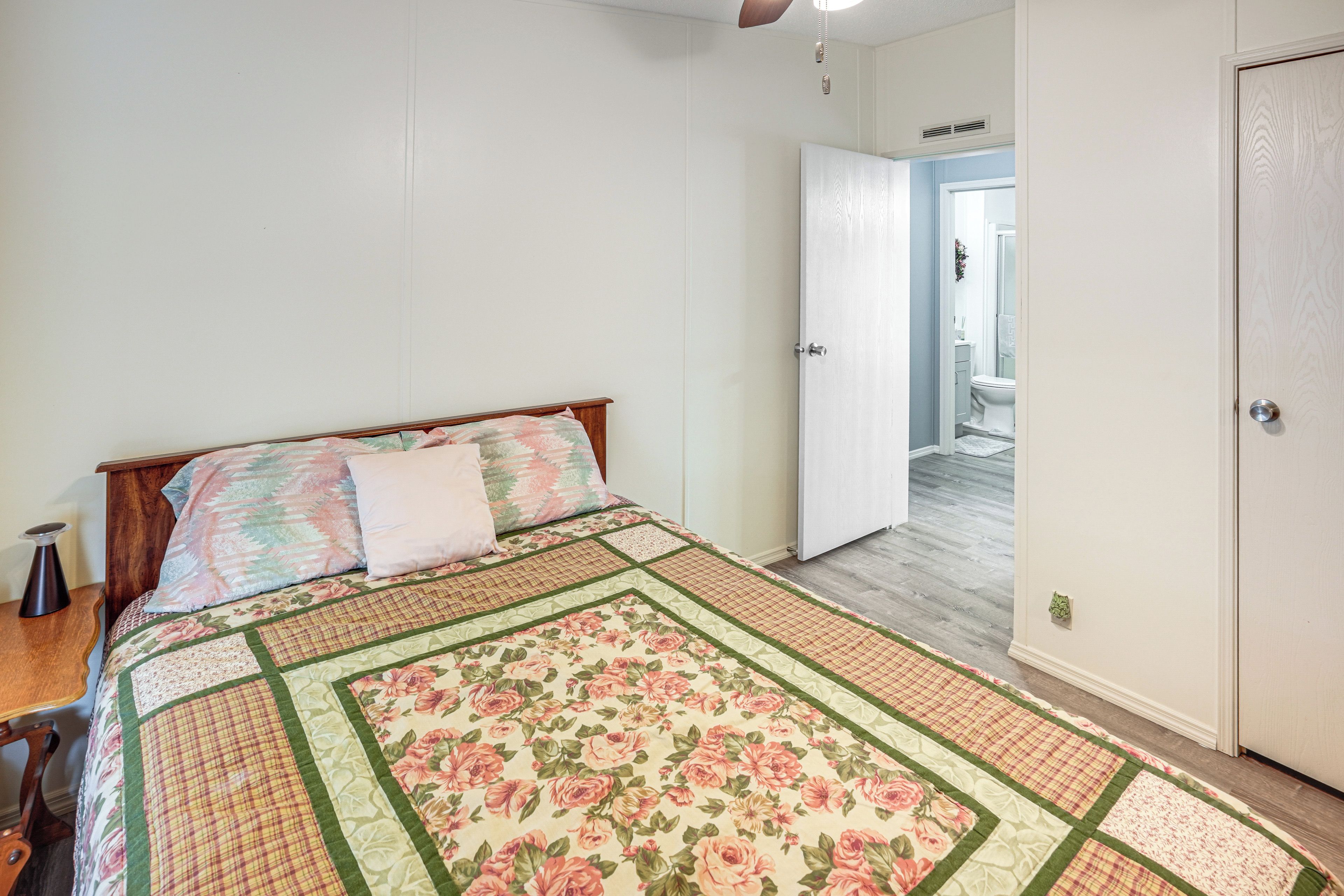Une chambre à coucher avec un lit, une table de chevet, une porte donnant sur une salle de bain et un plancher en bois.