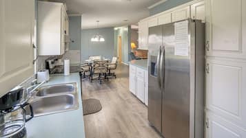 A modern kitchen with stainless steel appliances, a dining area with a table and chairs, and a hallway leading to a living space.