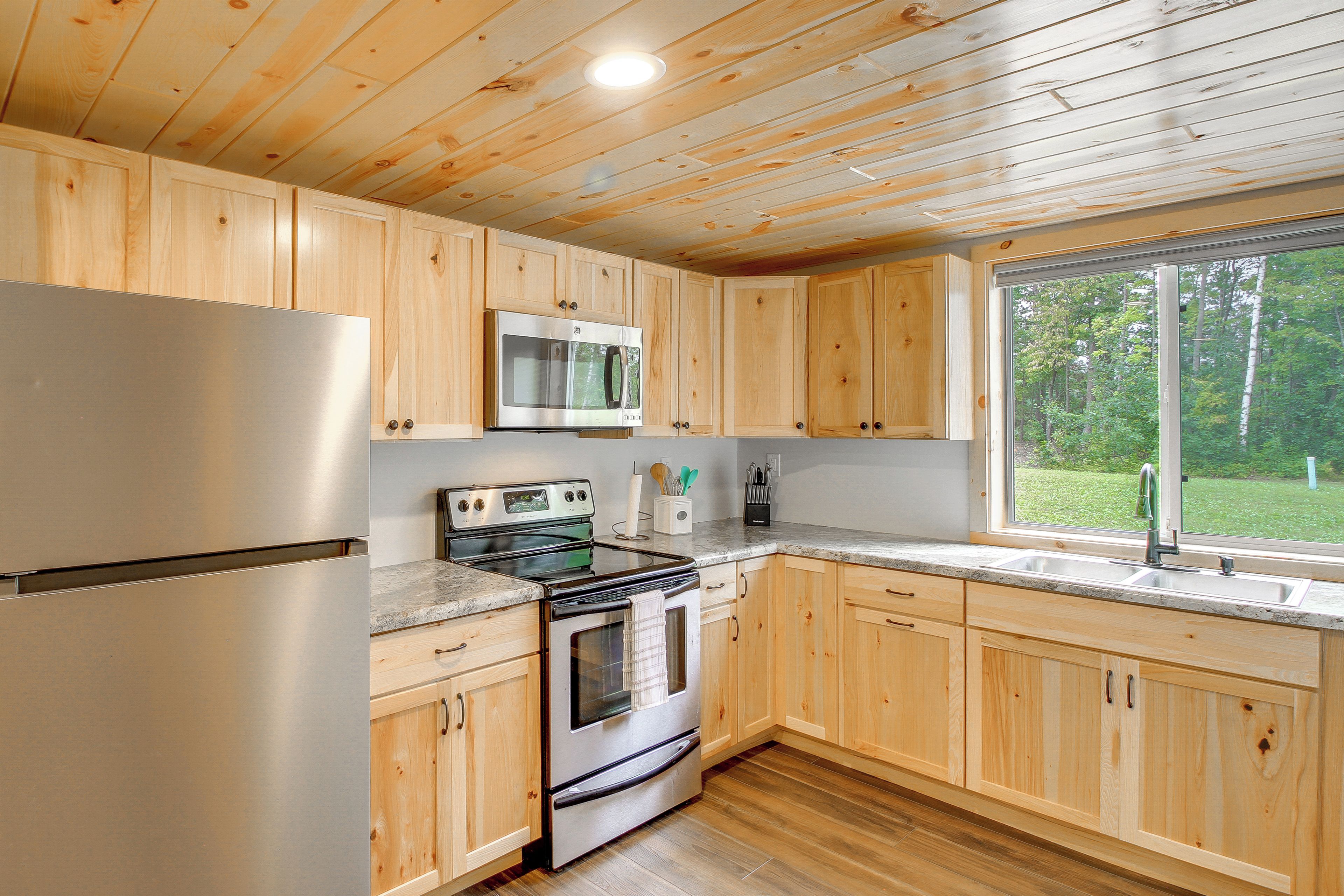 A kitchen with wooden cabinets, stainless steel appliances, and a window with a view of greenery.