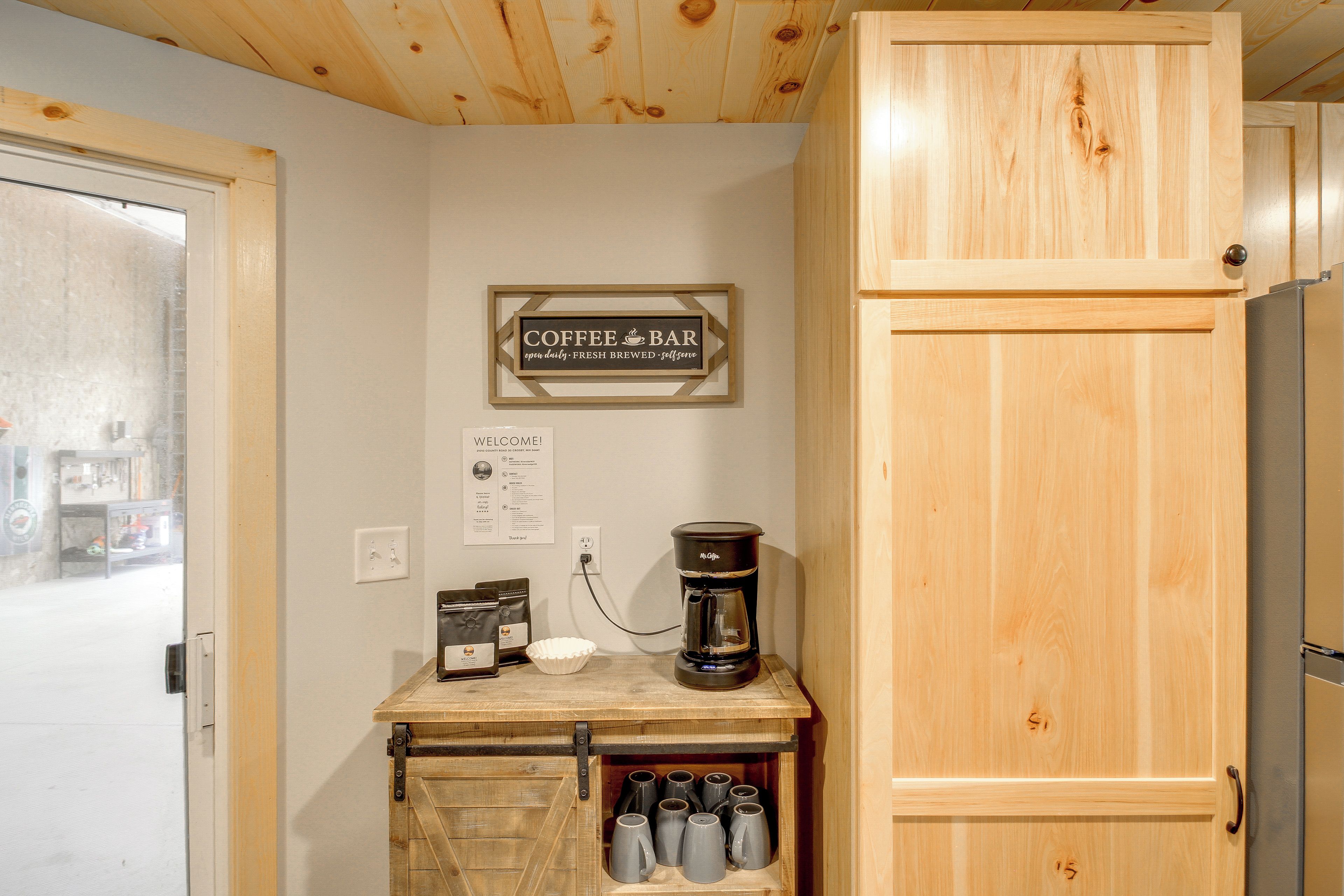 A kitchen with a coffee bar, a coffee maker, and mugs on a shelf.