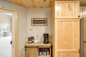 A kitchen with a coffee bar, a coffee maker, and mugs on a shelf.