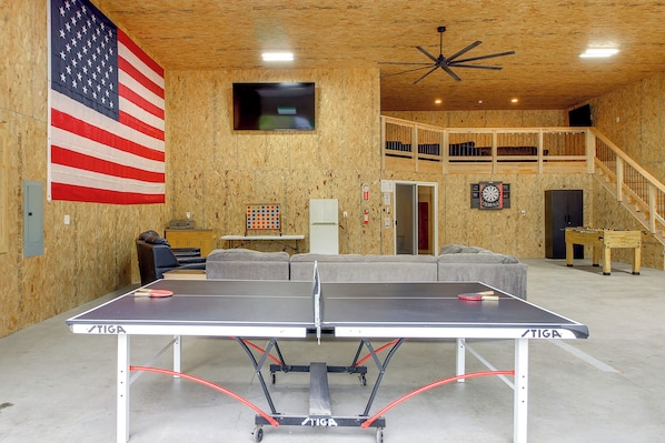 A ping pong table in a room with wooden walls, an American flag, a television, and a dartboard. - 'riverside Escape' Ride, Paddle, Relax (Crosby)