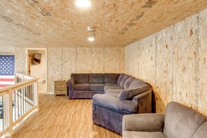 Um quarto com piso de madeira, sofá seccional, uma pequena mesa e uma bandeira na parede.