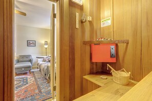 A sauna room with wooden walls, a red control panel, a bucket, and a wooden bench.