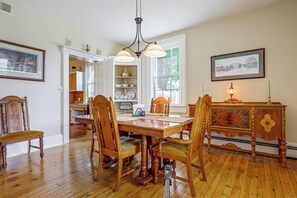 A dining room with a wooden table and chairs, a chandelier, and a cabinet with a decorative top.