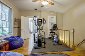A home gym with exercise equipment, a wooden floor, a ceiling fan, and a view of the outdoors through a window.