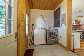 A laundry room with two washing machines, a drying rack, and a window with a view of greenery outside.
