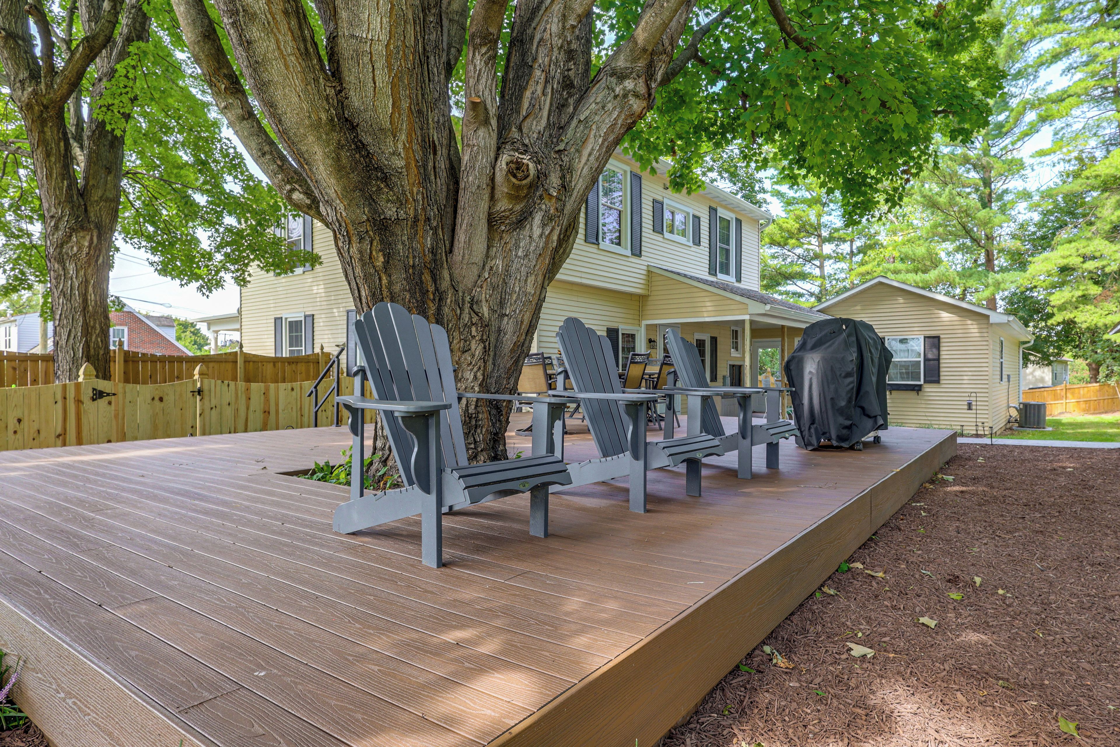 A deck with Adirondack chairs, a covered grill, and a house in the background.