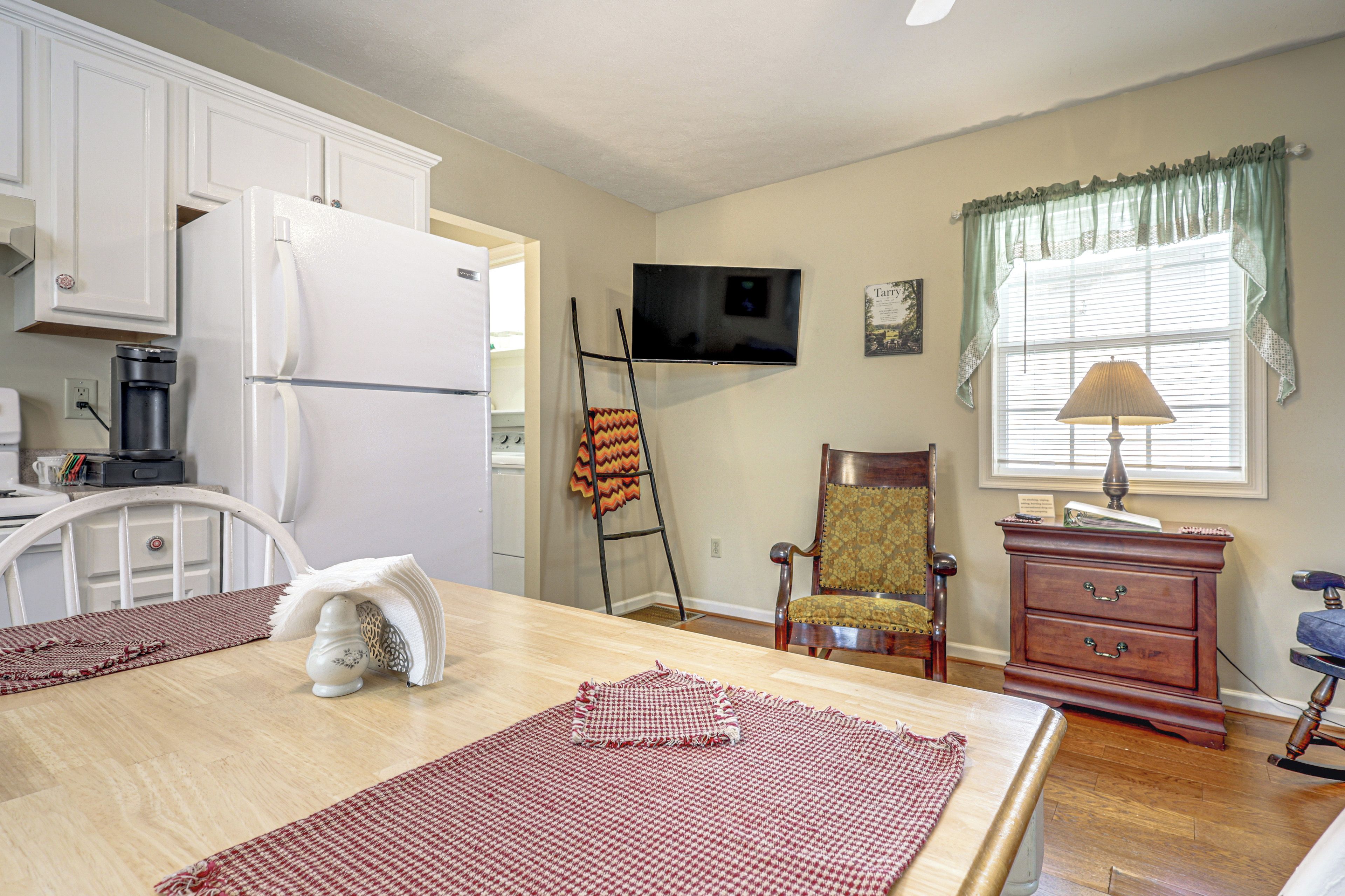 A kitchen with white cabinets, a refrigerator, a stove, a microwave, a television, and a window with curtains.