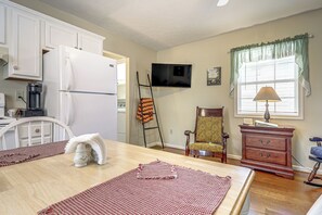 Eine Küche mit weißen Schränken, einem Kühlschrank, einem Herd, einer Mikrowelle, einem Fernseher und einem Fenster mit Vorhängen.