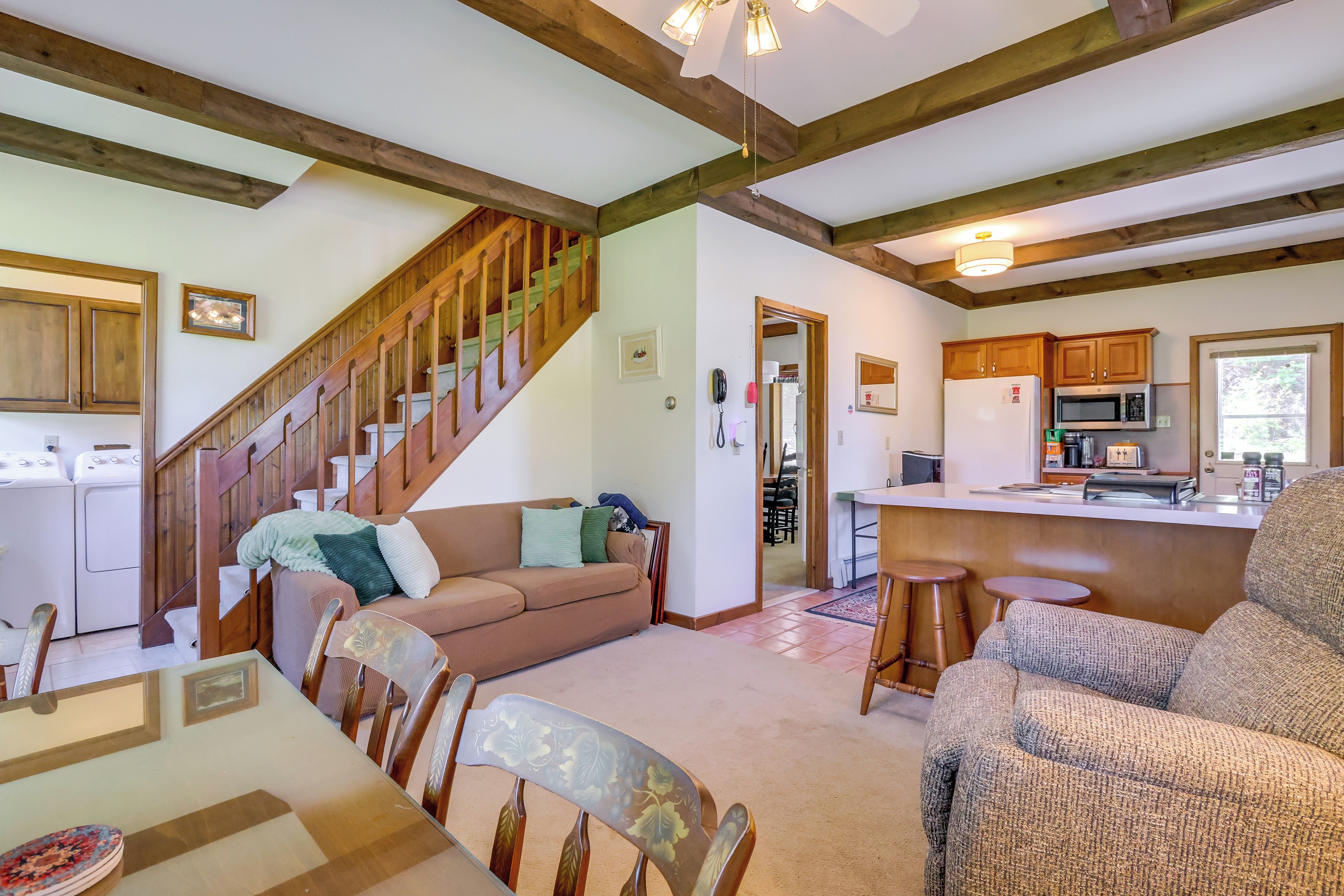A spacious living area with a wooden staircase, a kitchen with modern appliances, and a dining area with a table and chairs.