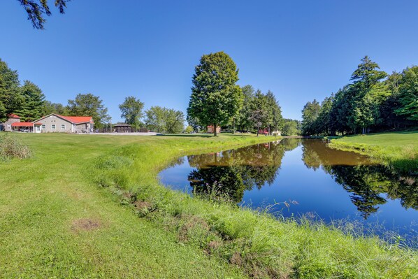 A serene landscape with a pond, grassy areas, and a building with a red roof. - Ride, Ski & Explore: Franklin, Vermont Getaway (Franklin)