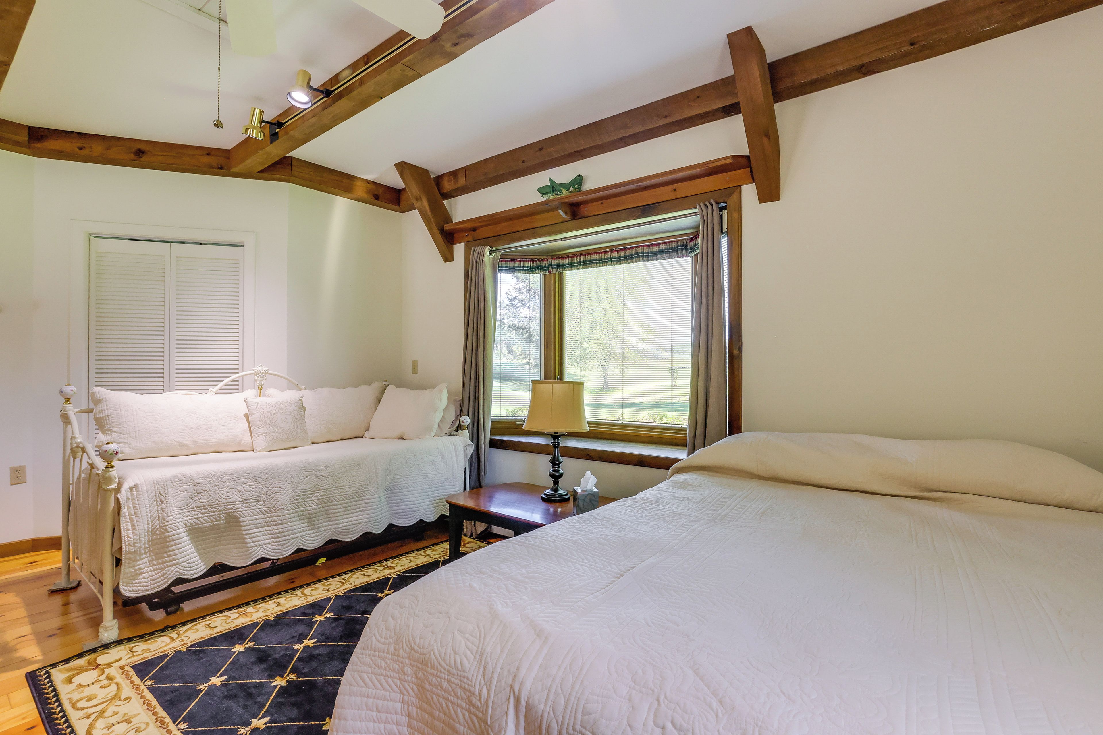 A bedroom with two beds, a window with curtains, a bedside table with a lamp, and a patterned rug.