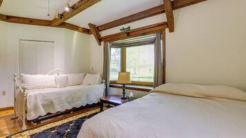 A bedroom with two beds, a window with curtains, a bedside table with a lamp, and a patterned rug.