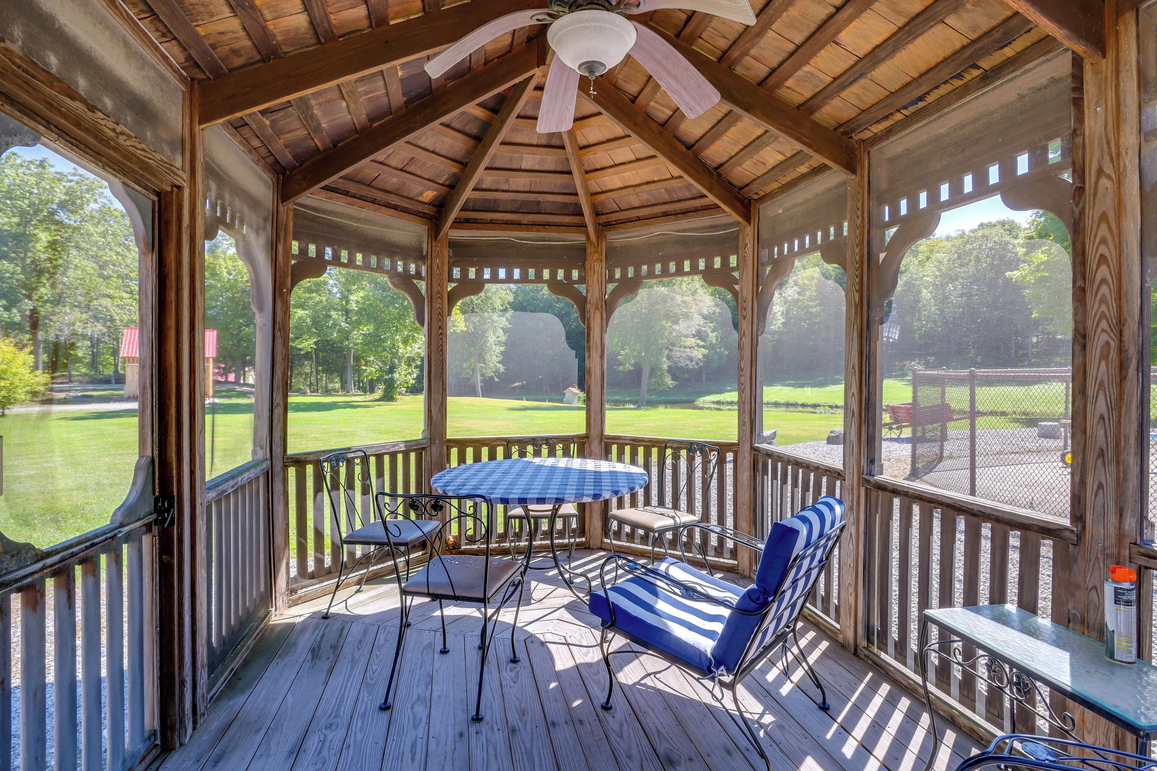 A covered outdoor area with a table and chairs, wooden flooring, and a view of a green landscape.