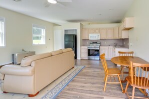 A modern kitchen with built-in appliances, a dining area with wooden chairs, and a beige sofa.