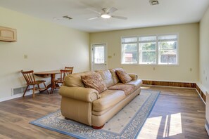 Un salon avec un canapé beige, des coussins décoratifs à motifs, une table à manger en bois avec des chaises et une grande fenêtre avec des stores.