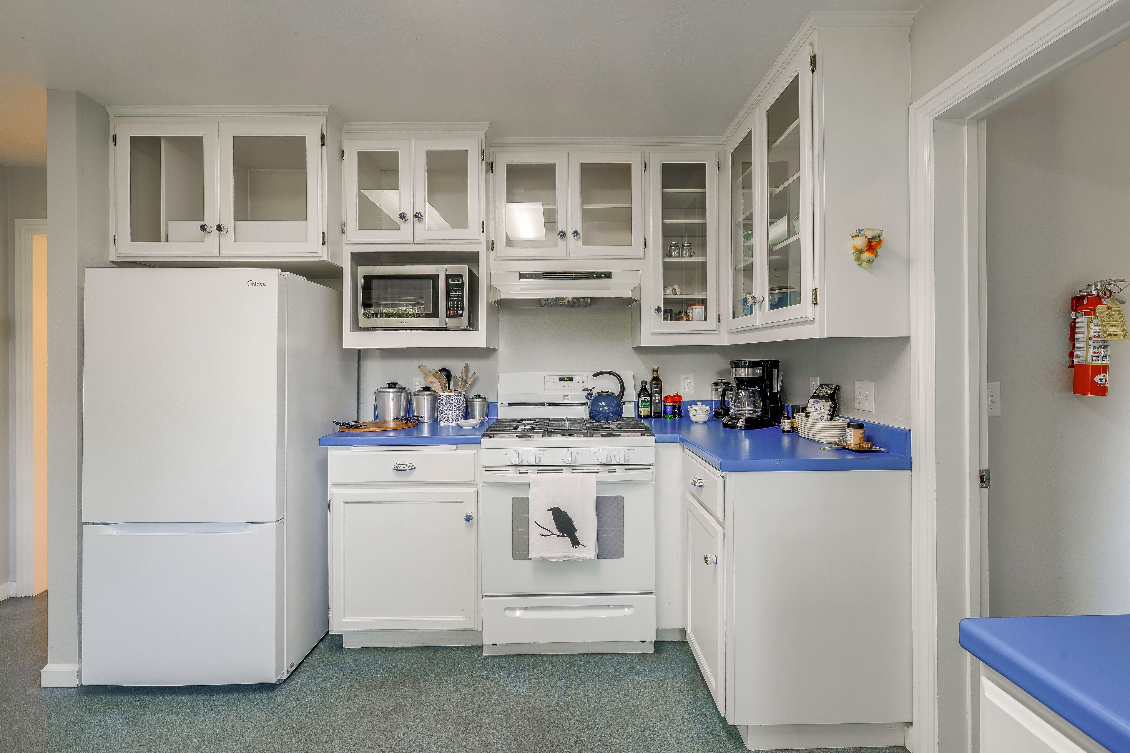 Une cuisine avec des meubles blancs, un réfrigérateur, un four à micro-ondes, une cuisinière et un évier.