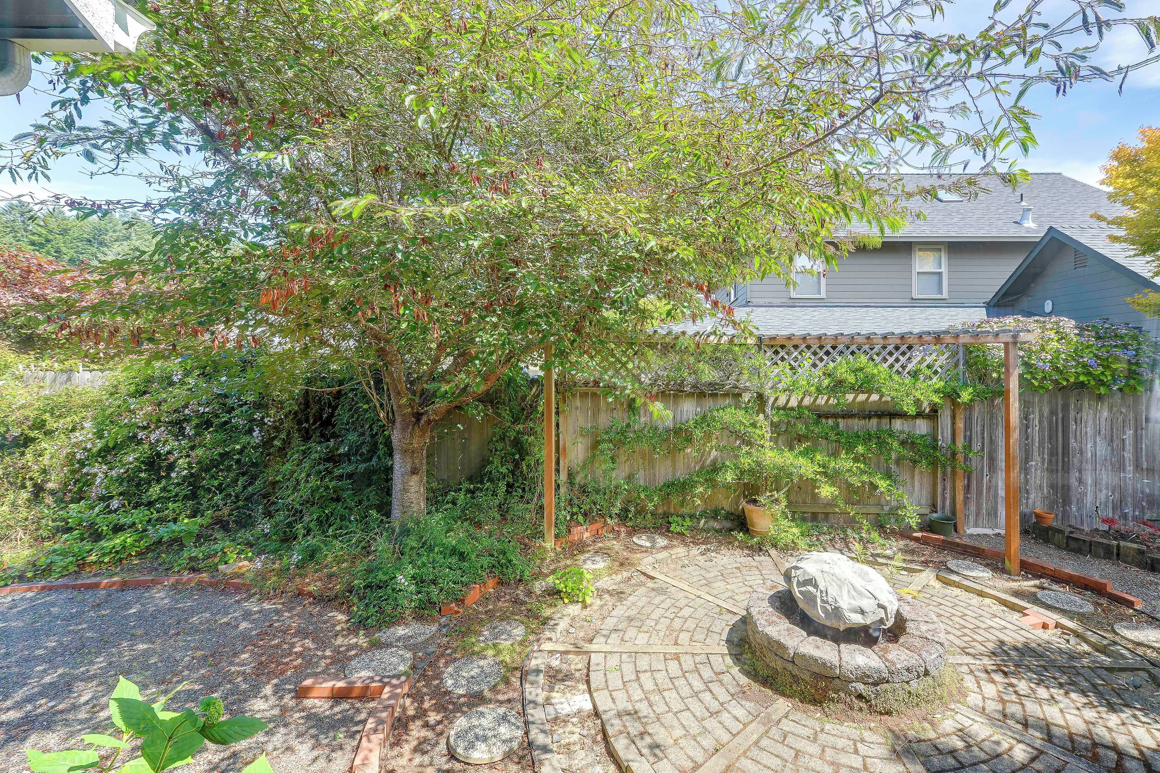 A backyard with a wooden pergola, a stone pathway, and a variety of plants and shrubs.