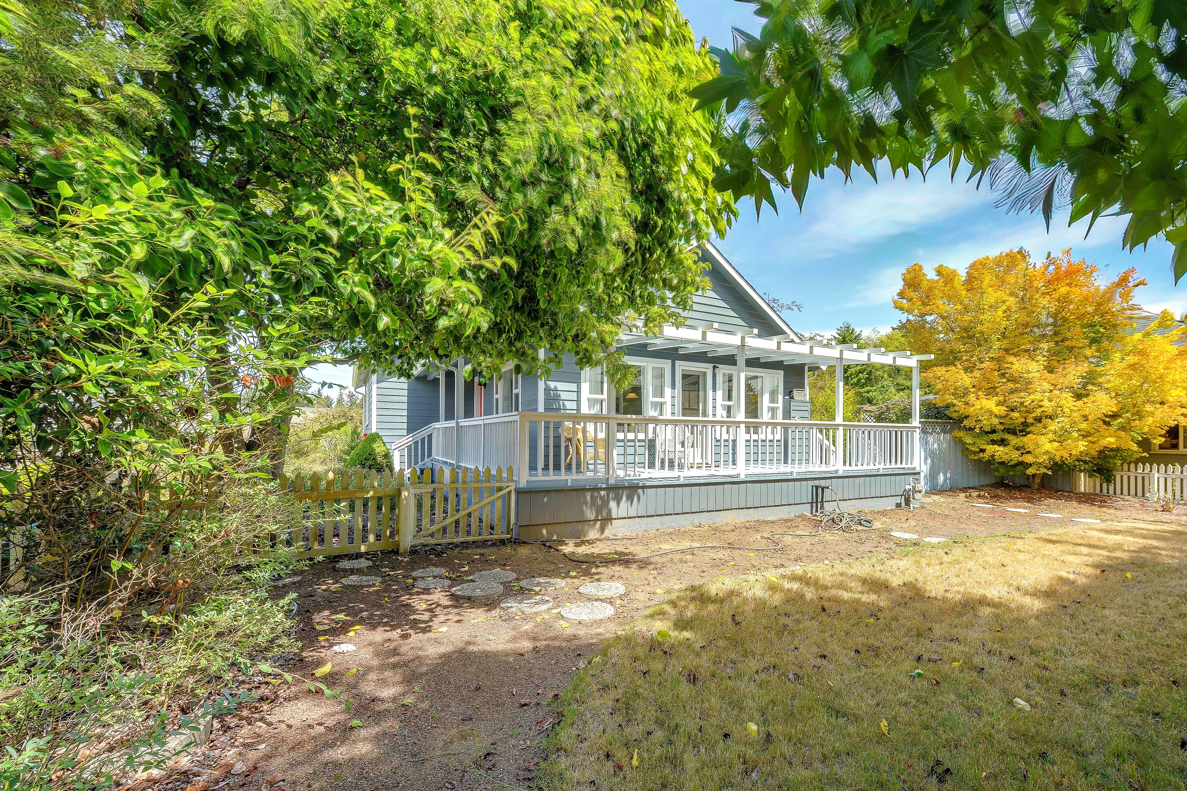 A residential property with a covered porch, a fenced yard, and a variety of trees.