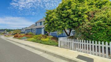 A residential street with a house, a white picket fence, and a variety of well-maintained gardens.