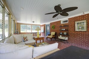 Uma sala de estar ampla com teto alto, ventilador de teto, parede de tijolos e uma grande janela.