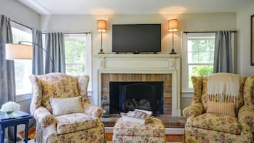 A living room with a fireplace, two armchairs, a side table, and a television above the fireplace.