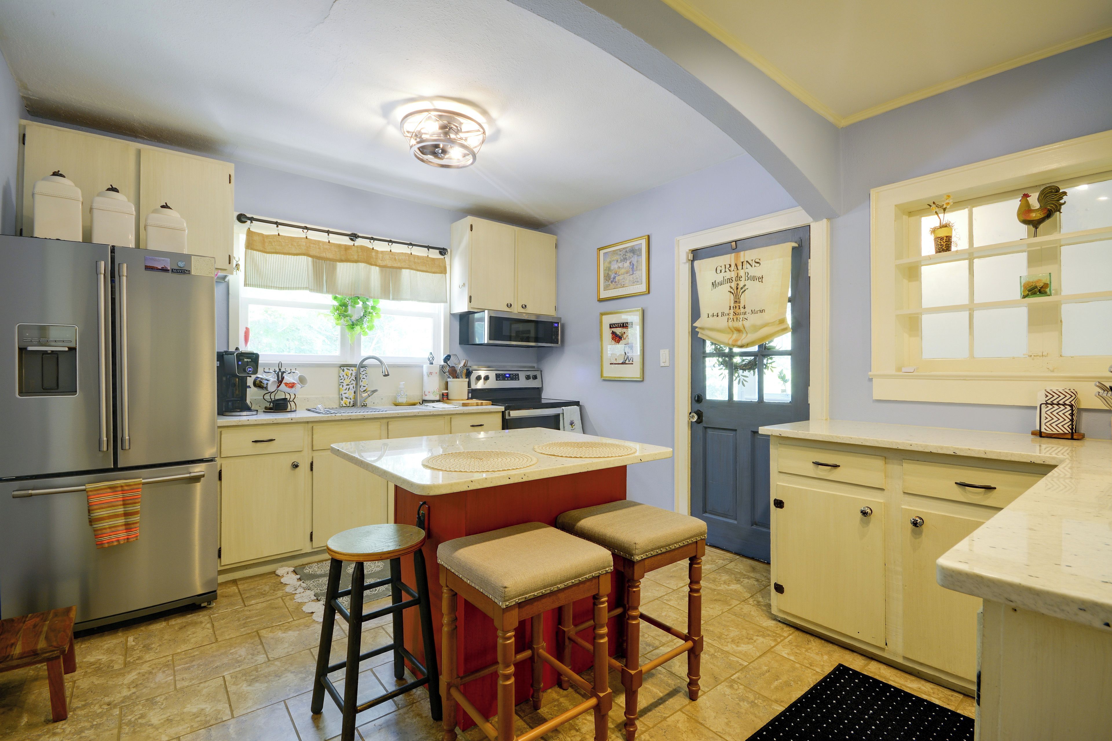 A kitchen with a central island, bar stools, a refrigerator, and a microwave.
