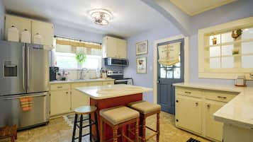 A kitchen with a central island, bar stools, a refrigerator, and a microwave.