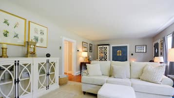 A living room with a white sofa, a white cabinet with glass doors, and framed botanical prints on the wall.