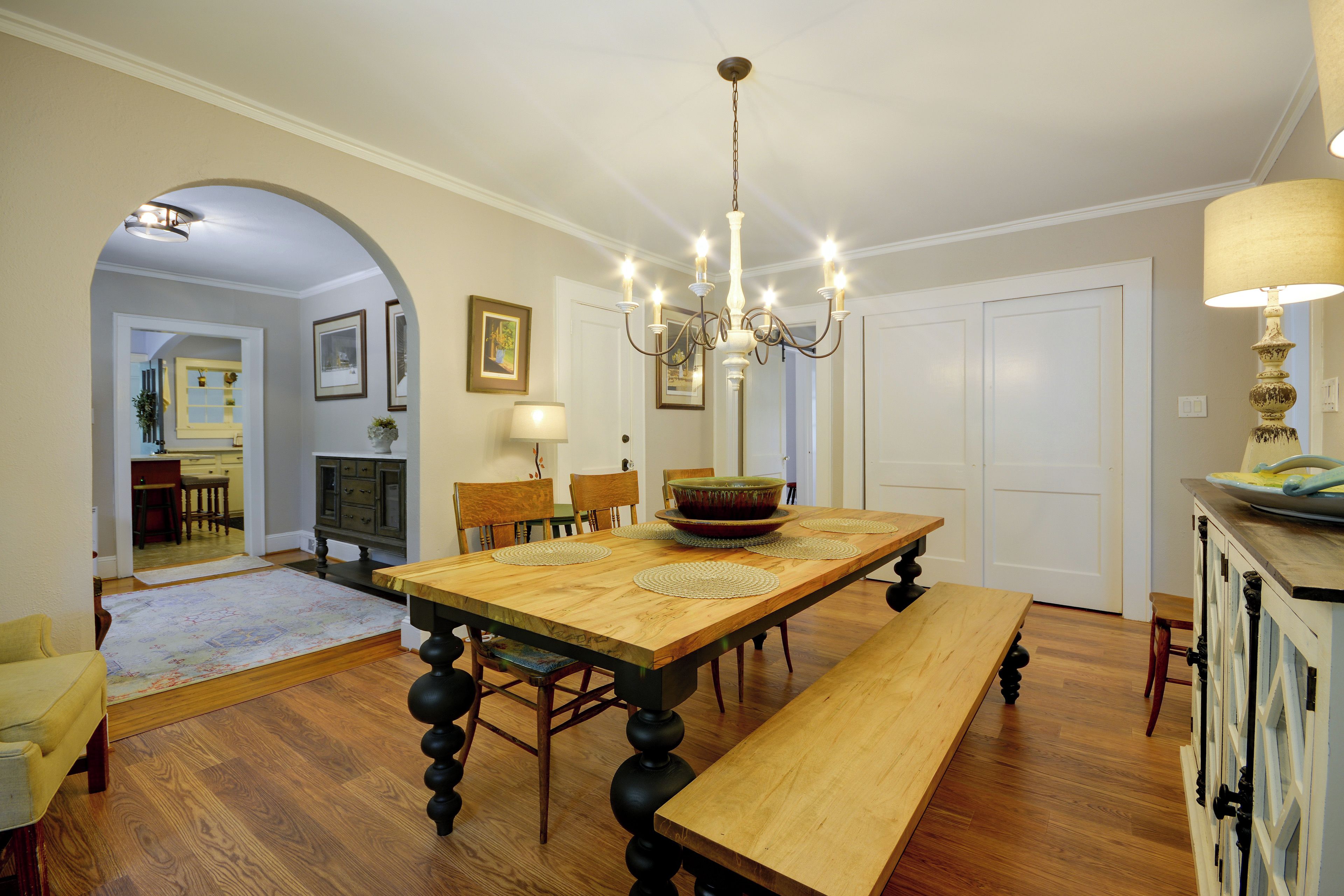 Un comedor con una mesa de madera, sillas, una lámpara de araña y un banco.
