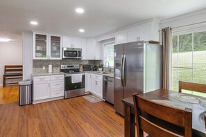 A modern kitchen with white cabinets, stainless steel appliances, and a wooden dining table. - Hickory Haven w/ Home Gym & Quiet Backyard Porch (Hickory)