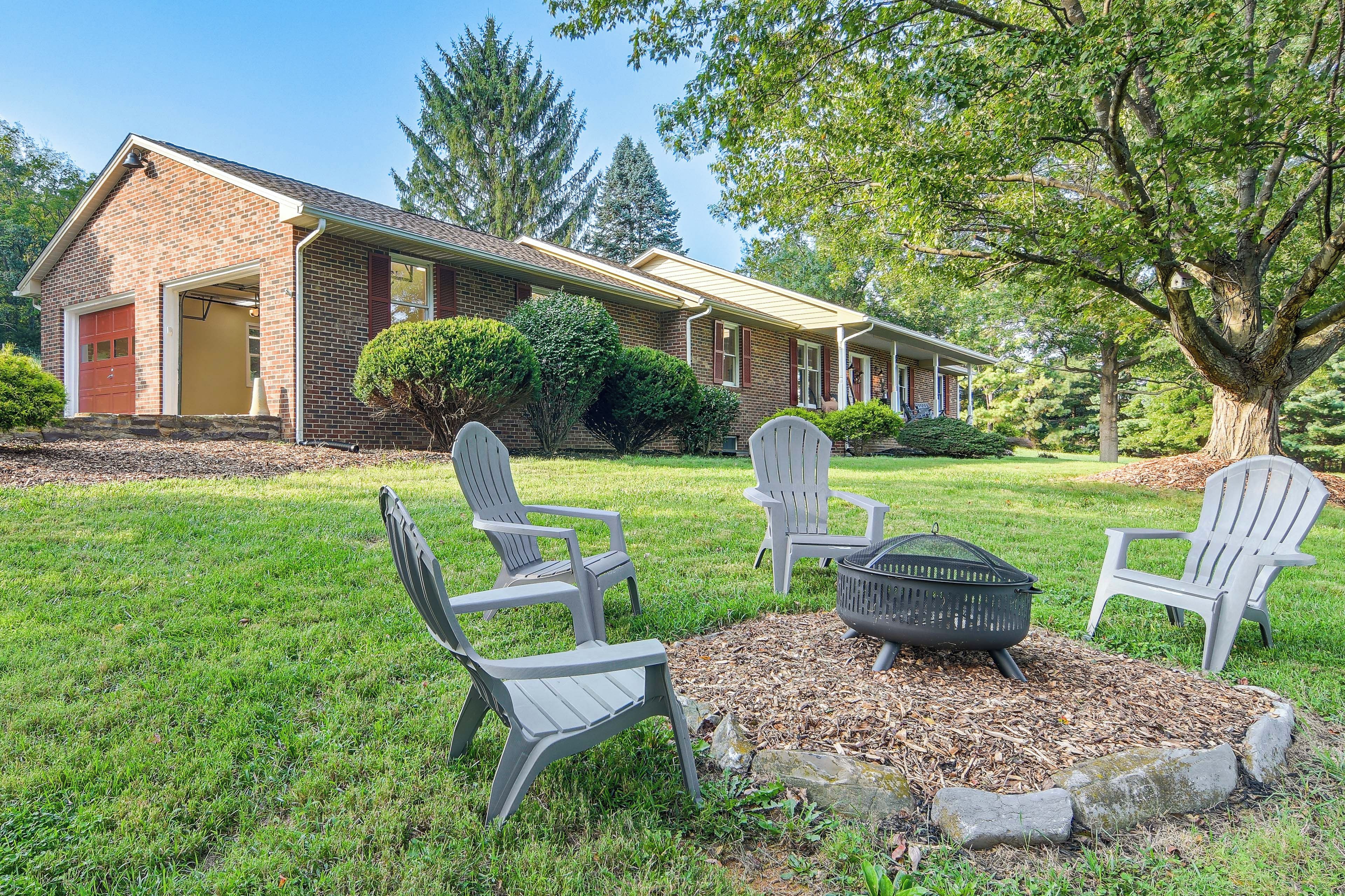 A brick house with a front porch, a fire pit, and Adirondack chairs.