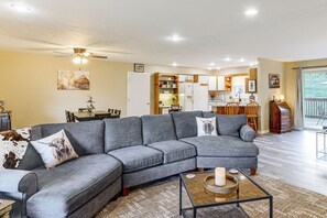 A modern living room with a sectional sofa, a dining area, and a kitchen with wooden cabinets. - Cozy Highland Cow Retreat - 4 Mi to JMU (Penn Laird)
