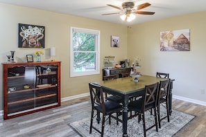 A dining area with a wooden table and chairs, a ceiling fan, and artwork on the walls. - Cozy Highland Cow Retreat - 4 Mi to JMU (Penn Laird)
