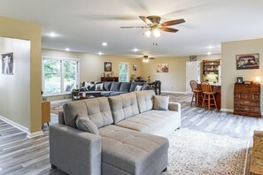 A spacious living area with a gray sectional sofa, a dining table with chairs, and a ceiling fan. - Cozy Highland Cow Retreat - 4 Mi to JMU (Penn Laird)