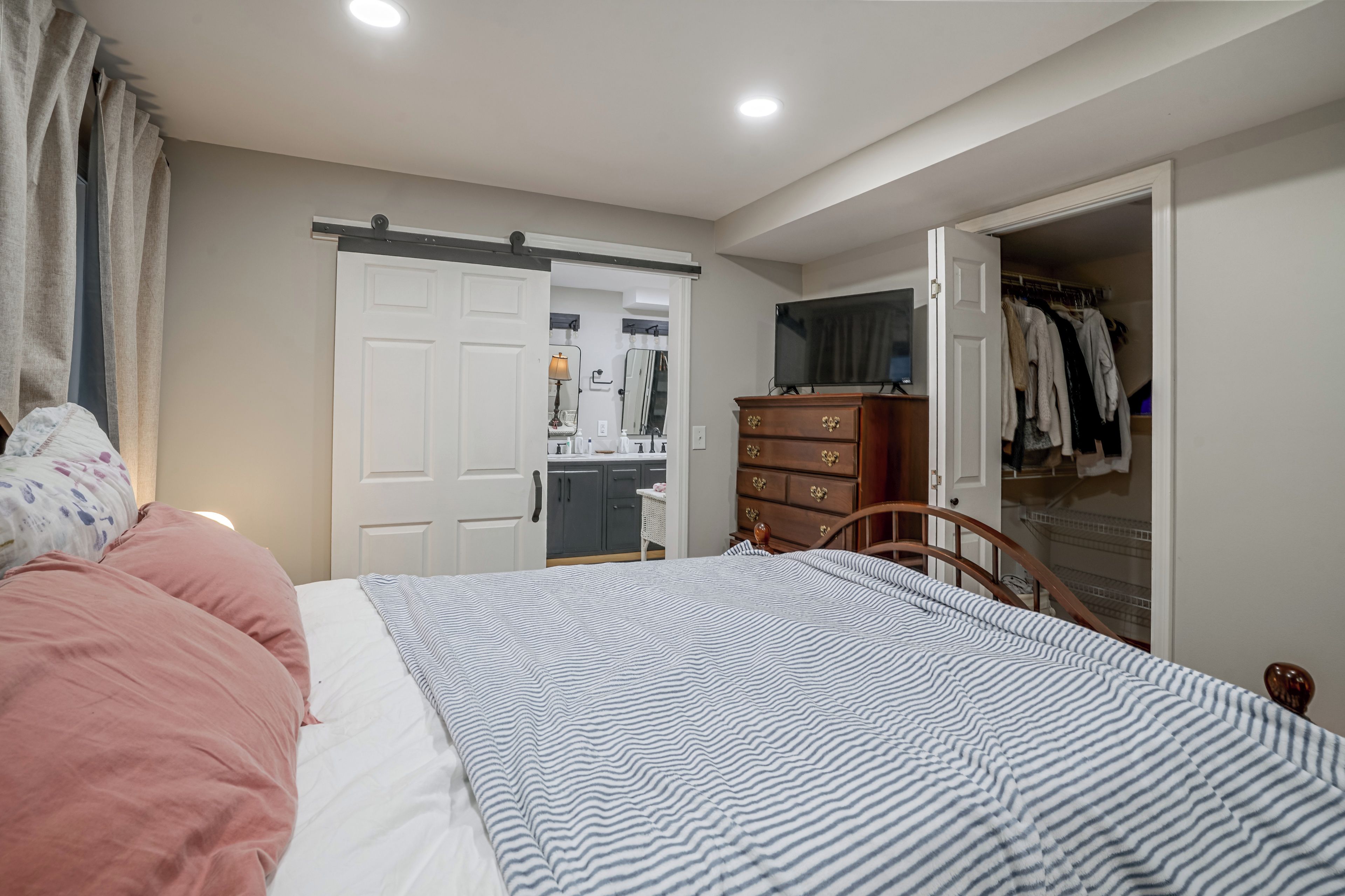 A bedroom with a bed, a dresser, a mirror, and a television.